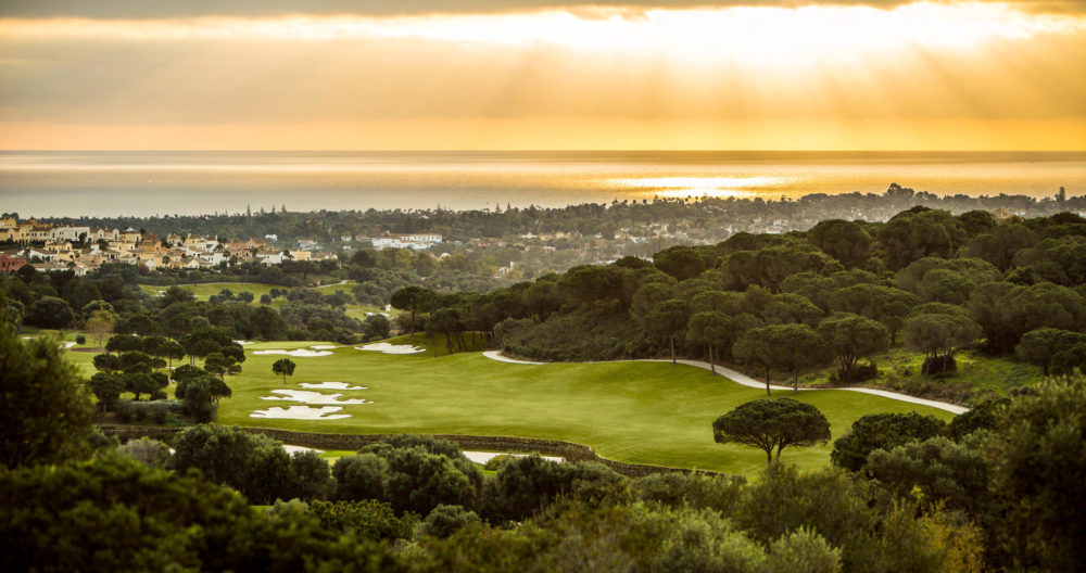 A golf course at sunset with a coastal town and the sea visible in the distance