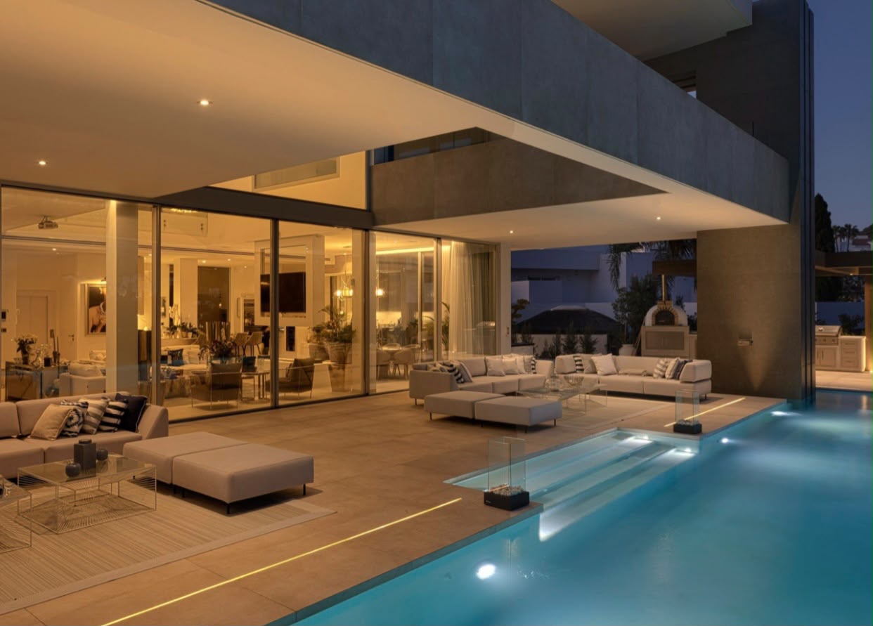 Pool terrace at dusk with lit interiors behind glass walls