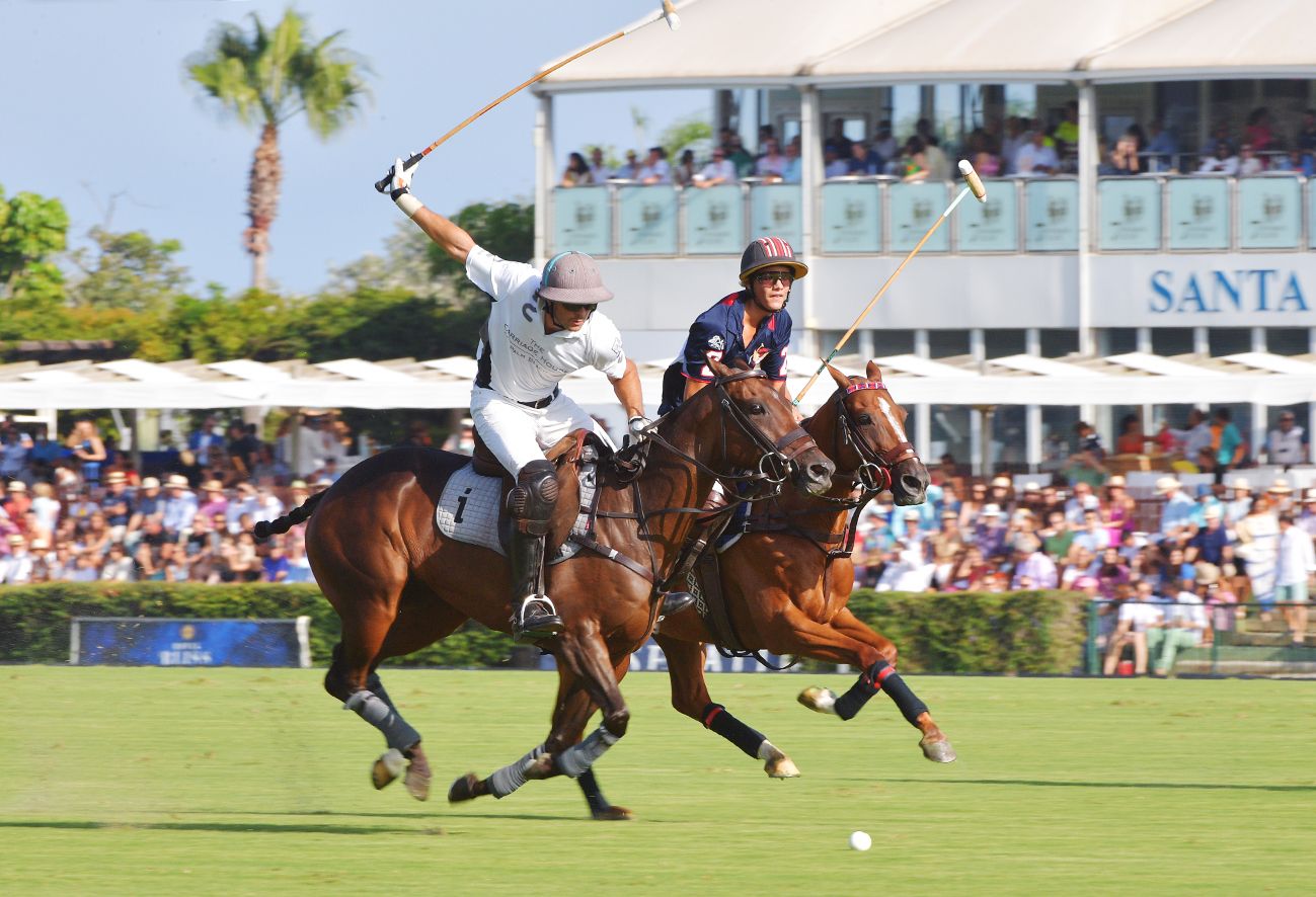 Two polo players on horseback contesting the ball during a match in front of a crowded grandstand